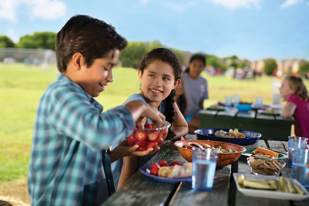 Childcare Programs YMCA staff member reading a book to two young boys while seated in a colorful activity room.